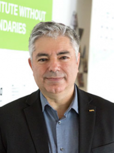 Man with grey hair wearing a blue shirt and blazer smiling at the camera.